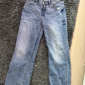 Baggy bootcut jeans från H&M - Baggy jeans från H&M med bootcut-ben och justerbar midja. De är ljusblå med slitningar och har klassisk femficksdesign. 