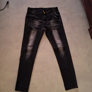 Svarta skinny jeans med slitningar - Svarta jeans från S.Oliver med skinny fit och coola slitningar framtill och baktill. Jeansen har en klassisk femficksdesign, orange knapp och tydliga tvättade detaljer som ger en snygg streetkänsla. Perfekta för dig som gillar en modern och edgy stil.