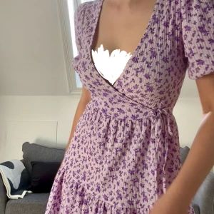 Ljuslila blommig omlottklänning - Perfekt sommarklänning. Har knappt använts. Vill du ej ha urringning rekommenderar jag att du har en bh-storlek under C och eventuellt B. Får superfin figur i den. 