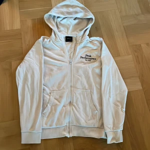 Peak Performance Hoodie | 160 - Snygg vit hoodie från Peak Performance med dragkedja och broderad logga på bröstet. Tröjan har huva, långa ärmar och två fickor framtill. Perfekt för chill dagar eller när du vill ha en clean look. Pris går att diskutera 