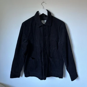 Svart manchester overshirt från H&M - Svart overshirt från H&M i mjuk manchester med klassisk krage, knäppning framtill och tre fickor. Jackan har raka långa ärmar med knapp vid mudden och är fodrad med polyester. Perfekt för lager-på-lager och chill stil. 3Y20
