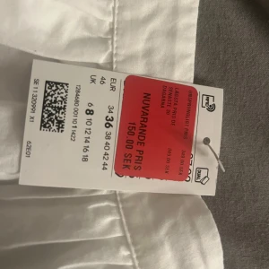 Vit broderad kortkjol i bomull - Superfin vit kortkjol från H&M i bomull med broderade blommor och vågig kant. Aldrig använt, prislapp kvar. För 120kr 