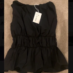 Svart volangig blus med resårmidja - Säljer en svart blus  med volangig nederdel och markerad resår i midjan. Jätte snygg och helt ny med prislapp på. Köpt för 435 kr. 