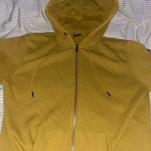 Gul hoodie med dragkedja från Colmar - Gul hoodie från Colmar Originals med hel dragkedja, huva med snörning och två fickor framtill. Mjuk insida och klassisk Colmar-logga på ärmen. Perfekt för dig som gillar streetwear och vill sticka ut med färg. Varm och skön perfekt för dig som vill chilla och vara varm. (Ny pris 2 000kr) 