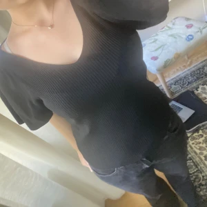 Svart ribbad topp med knyt i ryggen - Svart ribbad topp med v-ringning både fram och bak samt korta puffärmar. Toppen har en snygg knyt-detalj i ryggen som ger en extra touch. Materialet är stretchigt och sitter snyggt på kroppen. Perfekt för dig som gillar en enkel men ändå trendig look.