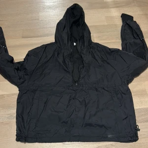 Svart vindjacka från Primark XS - Svart vindjacka från Primark i storlek XS. Jackan har huva, meshfoder och halv dragkedja framtill. Reflexprickar på ärm och rygg ger en cool touch. Justerbar nederkant med snörning. Perfekt för blåsiga dagar. Lite stor så passar bra en S 