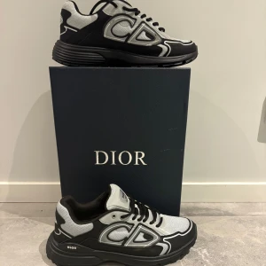 Dior B30 sneakers i svart och silver - Säljer ett par Dior B30 sneakers i svart och silver med coola reflekterande detaljer och tydlig CD-logga på sidan. Skorna har snörning, rund tå och en chunky sula. Ovandelen är i mesh och syntetmaterial för en modern vibe. Perfekta för dig som vill sticka ut med lyxig streetstyle.
