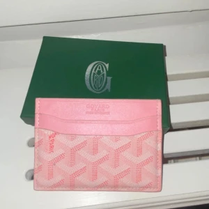 Rosa plånbok - Supersnygg rosa plånbok med ikoniskt mönster och flera kortfack. Tillverkad i skinn med klassisk logga och detaljer i ljusrosa. Perfekt för dig som vill ha något unikt och trendigt i väskan.