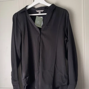 Svart glansig skjorta  - Svart skjorta från H&M i polyester, säljer för att den inte kommer till användning. Helt nytt skick!