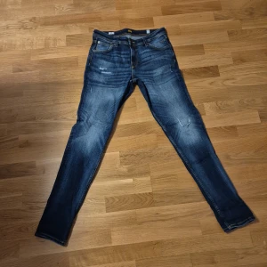 Jack & Jones skinny jeans blå - Snygga blå skinny jeans från Jack & Jones med slitningar och tvättade detaljer. Klassisk femficksmodell, gul kontrastsöm och dragkedja i gylfen. Passar dig som gillar en tajt och modern look. Perfekt till sneakers och hoodie.