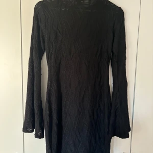 Svart långärmad klänning Boohoo - Svart klänning från Boohoo med lång ärm och coolt strukturerat mönster i tyget. Modellen är kort och har en rund halsringning. Perfekt för dig som gillar stilrena och trendiga plagg med lite edge.