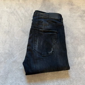 Svarta Perfect Jeans från Gina Tricot - Snygga svarta jeans från Gina Tricot, modellen Kristen Perfect Jeans. Jeansen har en mörk tvätt med lätt slitna detaljer och klassisk femficksdesign. De är tillverkade i stretchigt denim för en bekväm passform och har normal midja.