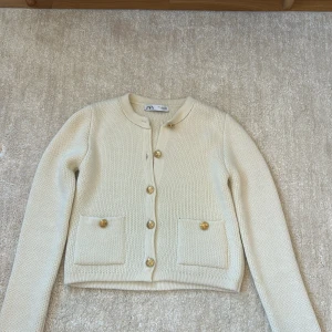 Beige kofta från Zara med guldknappar - Superfin beige kofta från Zara med snygga guldknappar framtill och på fickorna. Koftan är stickad, har rund halsringning och två fickor framtill. Perfekt för lager-på-lager och ger en clean och chic vibe.