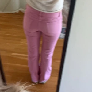 Ljusrosa bootcut jeans - Säljer ett par ljusrosa jeans med bootcut-modell och låg midja. Byxorna har klassisk femficksdesign och stängs med knapp och dragkedja. Perfekta för dig som vill sticka ut med färg och gillar en snygg passform.