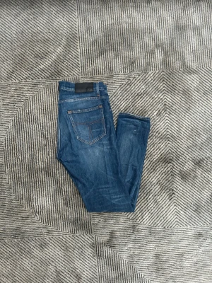 Blå jeans från Tiger of Sweden  - Snygga blå jeans från Tiger of Sweden med skinny passform och klassiska fem fickor. Jeansen har orange kontrastsömmar, låg midja och är tillverkade i stretchigt denim för extra komfort. Perfekta för dig som gillar en smal siluett och cool streetstil.