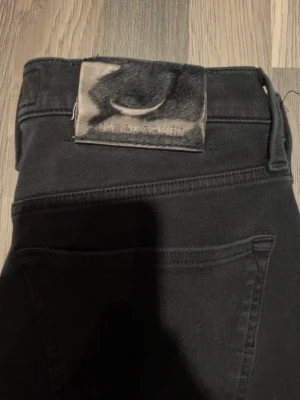 Svarta jeans från Jacob Cohën, stl 28 - Säljer ett par svarta jeans från Jacob Cohën i storlek 28. Byxorna har klassisk femficksdesign, raka ben och är tillverkade i ett mjukt bomullsmaterial med stretch. Snyggt Jacob Cohën-märke baktill och italiensk design. Perfekta för en stilren look. L32/W28 kostar typ 7000 nya