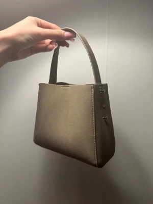 Beige handväska i mocka - Snygg beige handväska från Gina. Två små fläckar på ena sidan som man kan se på en av bilderna men märks knappt inte. Saknar axelbandet därav priset 