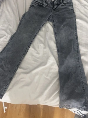 Grå jeans från Gina Tricot, storlek 158 - Säljer ett par grå jeans från Gina Tricot i storlek 158. De har en klassisk femficksdesign, utsvängda och normal passform. Jeansen är tillverkade i ett mjukt denimtyg och har snygg tvättad look med mörkgrå ton. Perfekta för dig som gillar stilrena och enkla jeans.