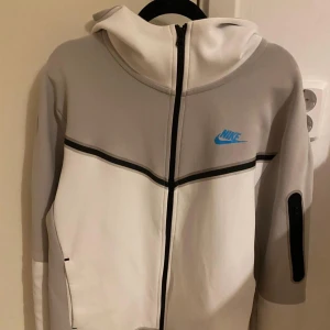 Nike hoodie i vitt och grått med blå logga - Hej Nike hoodie i vitt och ljusgrått, har köpt den men trodde hade M vilket ej ja hade jag har S och det finns ingen skador endast använda ett fåtal gng bara den är nästan som ny bara hör av er vid frågor. PRIS KAN SJÄLVKLART DISKUTERAS!! 🔥 