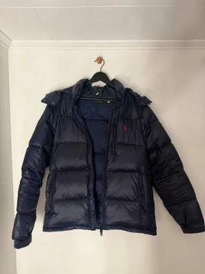 Mörkblå pufferjacka från Polo Ralph Lauren - Säljer en mörkblåpuffer jacka i storlek M från Polo Ralph Lauren i mycket fint skick. Jackan är knappt använd och ser i princip ut som ny. Vid fundering eller om du vill ha fler bilder på jackan eller passformen så är det bara att skriva😁