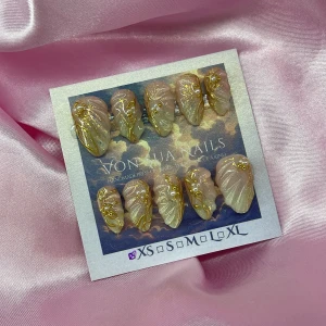 DawnOcean (XS); Short Almond;Curved - Säljer ett set med handgjorda press-on naglar i storlek XS: 14 mm, 11 mm, 11,5 mm, 10 mm, 8 mm. Naglarna har en nude-rosa bas med skimrande finish och detaljer i guld, inklusive mönster och pärlliknande accenter. Formen är kort almond, Perfekt för dig som vill ha unika och glamorösa naglar.