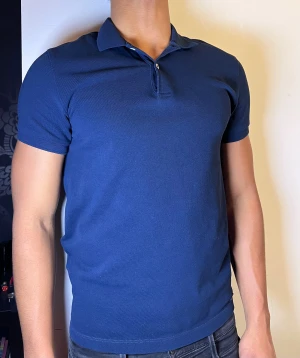 Marinblå pikétröja från Massimo Dutti - Säljer en stilren marinblå pikétröja från Massimo Dutti. Tröjan har klassisk krage, korta ärmar och två knappar vid halsen. Materialet är mjuk bomull som känns skönt mot huden och ger en snygg passform. Perfekt för dig som gillar enkel och clean stil.