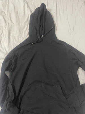 Svart hoodie från 157, storlek XL - Svart hoodie från 157 i storlek XL. Klassisk modell med huva och snörning, samt stor magficka framtill. Mjuk insida och ribbade muddar vid ärmslut och nederkant. Perfekt för chill dagar eller när du vill ha något bekvämt och enkelt.