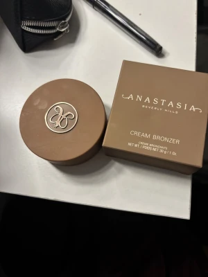 Anastasia Beverly Hills Cream Bronzer Caramel - Säljer en Anastasia Beverly Hills Cream Bronzer i färgen Caramel. Krämig formula som smälter in i huden och ger en naturlig solkysst look. Kommer i en rund burk med skruvlock och ikonisk ABH-logga. Perfekt för contouring eller värme till ansiktet.