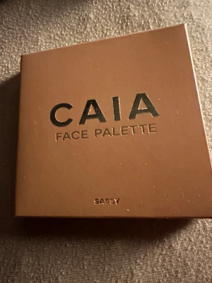 CAIA Face Palette Sassy - Snygg ansiktspalett från CAIA i färgen Sassy. Paletten innehåller bronzer, rouge, contour och highlighter i kompakta puderform. Brun förpackning med stilren design, perfekt för att skapa en fräsch och definierad look. Tillverkad i Italien.Helt Ny oöppnad palett 