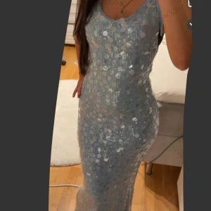 Ljusblå glittrig långklänning med öppen rygg - Supersnygg ljusblå långklänning med stora paljetter som glittrar. Klänningen har halterneck, öppen rygg med knyt och figurnära passform. Perfekt för dig som vill sticka ut och glänsa på festen!