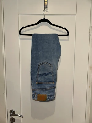 Nudie Jeans ljusblå skinny jeans 34/30 - Säljer ett par Nudie Jeans i ljusblå tvätt med klassiska bakfickor och orangea sömmar. Modellen är skinny med normal midja och raka ben. Jeansen har fem fickor och är tillverkade i mjukt bomullsmaterial för skön passform.