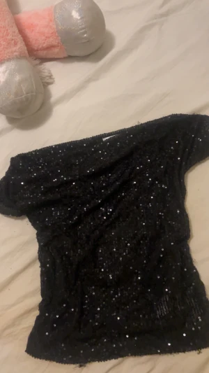 Svart glittrig offshoulder topp Gina Tricot - Svart offshoulder topp från Gina Tricot, täckt med glittriga paljetter som ger en riktigt festlig vibe. Den har inbyggt linne och sista bilden är när ja har kjol också så tröjan är inte så lång 