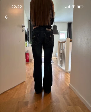 True Religion mörkblå bootcut jeans - Säljer ett par mörkblå jeans från True Religion med bootcut passform och låg midja. Jeansen har snygga kontrastsömmar, klassiska fickor med lock och silverfärgad knapp framtill. Märkespatch bak och detaljerad design på bakfickorna.