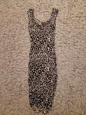 Leopardmönstrad kort klänning H&M XS - Säljer en snygg, tight leopardmönstrad klänning från H&M i storlek XS. Klänningen är kort, har breda axelband och är i beige och svart. Perfekt för dig som vill sticka ut med ett djurmönster och gillar figurnära passform.