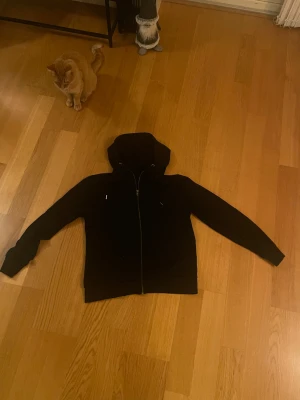 Svart zip hoodie med dragkedja från 157 - Svart hoodie från 157 i storlek M. Klassisk modell med huva och dragsko, hel dragkedja framtill och långa ärmar. Mjuk insida och enkel stil som funkar till det mesta. Perfekt för chill eller häng med kompisar.