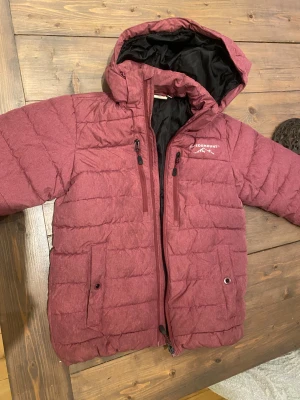 Mörkröd pufferjacka från Swedemount - Säljer en mörkröd pufferjacka från Swedemount med huva och svarta detaljer på insidan. Jackan har två bröstfickor med dragkedja och två stora fickor framtill. Perfekt för kalla dagar och har en riktigt skön passform.