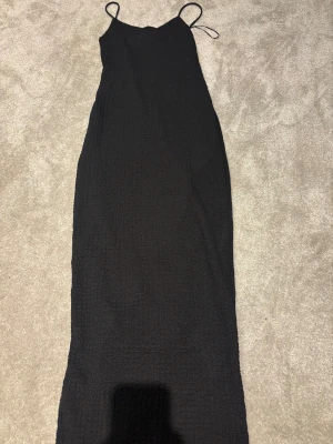 Svart långklänning från Sister XXS - Supersnygg svart långklänning från Sister i storlek XXS. Använd 1 gång (har andra klänningar så har inte använt den.) Klänningen har smala axelband och är tillverkad i ett strukturerat, lätt stretchigt material som ger en cool textur. Enkel och stilren design med figurnära passform, perfekt för dig som gillar minimalistisk stil.