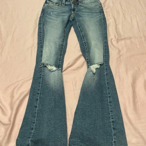 Blå bootcut jeans  - Snygga blå bootcut jeans med slitna detaljer på knäna och coola broderade bakfickor. Jeansen har klassisk femficksdesign, låg midja och är tillverkade i mjukt denimtyg. Perfekt för dig som gillar najs vibbar och snygga jeans.