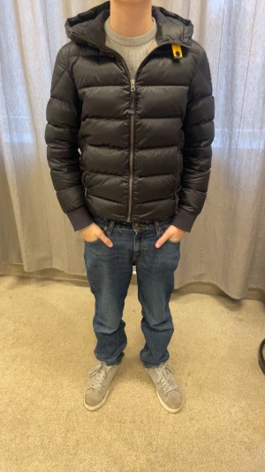 Svart dunjacka Parajumpers Sheen - Svart dunjacka från Parajumpers, modell Sheen. Jackan har huva, ribbade muddar och en gul detalj vid kragen. Insidan är ljusgrå och jackan har dragkedja framtill samt patch på ärmen. Perfekt för kalla dagar och har en clean, sportig look. Storleken är Y-M, jag är 167 och som ni ser på bilderna sitter den perfekt. Pris kan diskuteras vid snabb affär