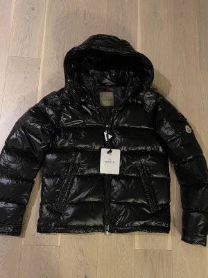 Moncler Maya jacka - Säljer en helt ny och oanvänd Moncler Maya dunjacka i svart, komplett med alla tillbehör. Storlek 1/S. Jackan levereras med samtliga etiketter, tags och Monclers autenticitetsbricka. Både QR-kod, NFC och RFID-tagg fungerar och länkar dig direkt till Monclers officiella hemsida. Perfekt som julklapp eller till dig som vill ha en varm, lyxig och tidlös vinterjacka från ett av världens mest exklusiva märken. #Moncler #MonclerMaya #Dunjacka #Lyxmärke #Designerjacka #Vinterjacka #Fashion #Streetwear 