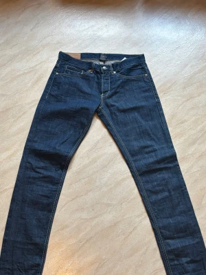 Mörkblå dondup george jeans  - Snygga mörkblå jeans från dondup med raka ben och tydliga kontrastsömmar. Klassisk femficksmodell och läderpatch med logga bak. Jeansen har normal passform och är tillverkade i slitstarkt denimtyg. Perfekta för dig som gillar stilrena och tidlösa jeans.