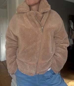 Beige oversized teddyjacka med dragkedjor NA-KD stl.L - Supermjuk och fluffig teddyjacka i beige med oversized krage och snedställd dragkedja framtill. Jackan har coola detaljer som dragkedjor vid ärmslut och fickor. Perfekt för dig som vill ha en varm och trendig look under höst och vinter. Fint skick från märket NA-KD. Stl.42/L. Jag är en S men gillar den oversized.