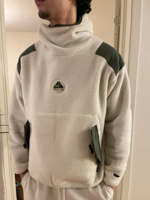 Nike Acg fleece balaclava pullover jacka - Nike ACG fleece balaclava pullover jacka i strl L. Original. Vit och khakigrön. Orginalpris 2250 kr.