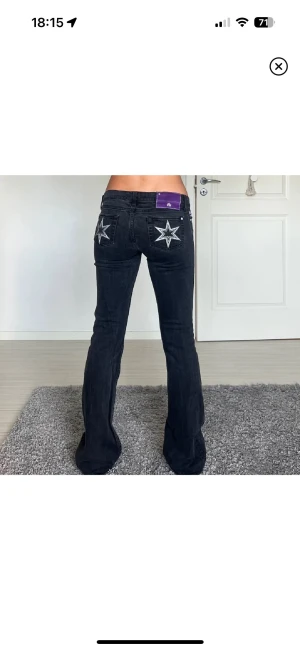 Victoria Beckham jeans - Snygga svarta jeans från Victoria Beckham med bootcut passform och låg midja. Baktill finns broderade vita stjärnor på bakfickorna och ett lila patch vid linningen. Jeansen är i klassisk denim och har en cool, unik look. W27 L34! 40cm rakt över och 84 i innerbenslängd❤️