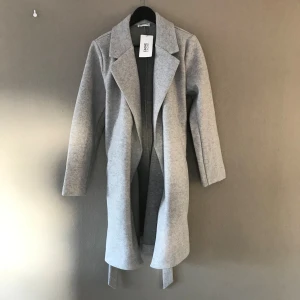 Grå kappa storlek 40. Oanvänd.  - Fin kappa med knytband. Aldrig använd, har lappen kvar. Lite åt det tjockare hållet. Storlek 40 / medium. 