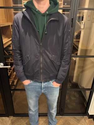 Woolwich bomberjacka mörkblå - Säljer en mörkblå bomberjacka från Woolrich i storlek L. Tillverkad i polyester med klassisk bomberkrage och ribbade muddar. Bra skick, inga defekter hittade! Skön passform och storleken är L men passar större M också! Pris: 1299kr