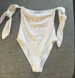 Vit baddräkt med knyt från Ivyrevel - Supersnygg vit baddräkt från Ivyrevel med breda axelband som knyts i stora rosetter. Klassisk, enkel design med hög skärning vid benen och rak ringning. Tillverkad i stretchigt material som sitter bekvämt och smickrande.