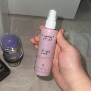 Lumene Dewy Glow Setting Spray - Lumene Invisible Illumination Dewy Glow Setting Spray i en ljusrosa plastflaska med vit spraypump. Ger lyster och återfuktning till huden, perfekt för att fixera sminket. Innehåller 100 ml och passar alla hudtyper. Skandinavisk design och vegansk formula.