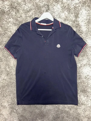 Moncler Navy Piké Tröja - Stilren navy piké från Moncler. Några fläckar på framsidan men annars i väldigt bra skick. Perfekt plagg men sommaren är över så den får gå vidare. Skick: 8/10 Pris kan diskuteras 📦 Skickas eller möts upp