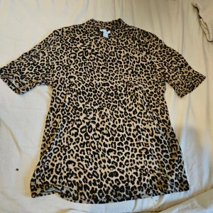 Leopardmönstrad t-shirt  - Säljer en kortärmad t-shirt med leopardmönster i beige och svart. T-shirten har en klassisk rund hals och är gjord i mjuk bomull, perfekt för dig som gillar att sticka ut med djurprint. Passar dig som vill ha en cool och trendig look.